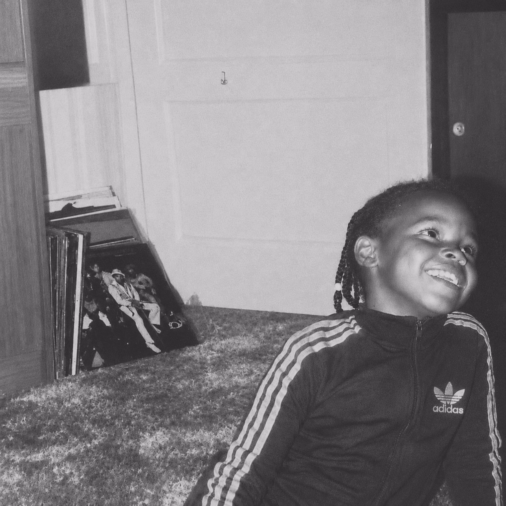 Little Miss Renee as a child in an Adidas jacket, smiling beside a stack of vinyl records